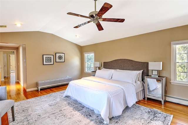 bedroom with lofted ceiling, multiple windows, a baseboard radiator, and wood finished floors