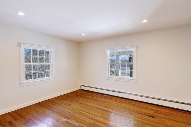 empty room featuring a baseboard heating unit, recessed lighting, baseboards, and wood finished floors