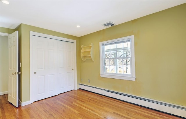 unfurnished bedroom featuring visible vents, baseboards, light wood-style floors, baseboard heating, and a closet