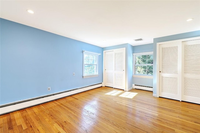 unfurnished bedroom featuring light wood-style floors, visible vents, a baseboard heating unit, and two closets