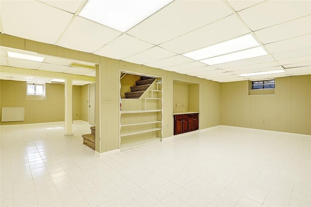 basement with built in features, a paneled ceiling, and stairway