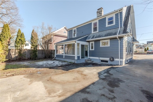 back of house featuring a shingled roof, a gambrel roof, a sunroom, a chimney, and fence