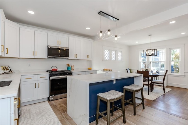 kitchen with a center island, light wood finished floors, stainless steel appliances, white cabinets, and a kitchen bar