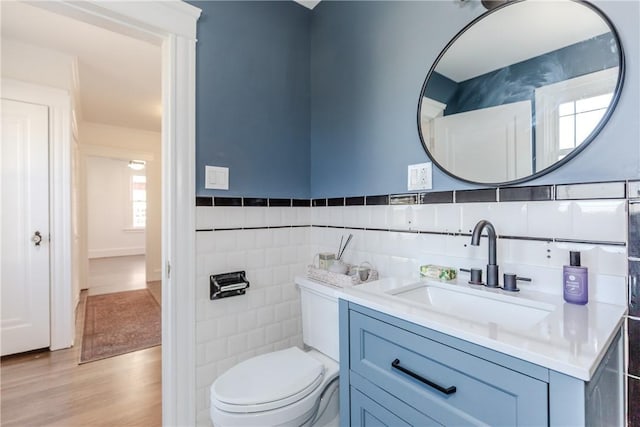 half bathroom with toilet, wood finished floors, vanity, tile walls, and wainscoting