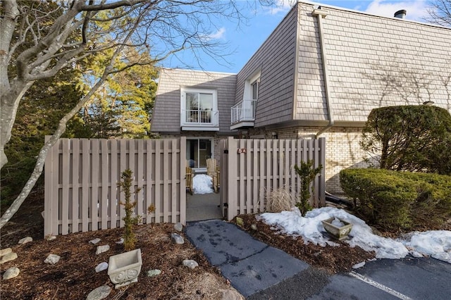 view of property exterior featuring mansard roof, a balcony, a fenced front yard, a gate, and brick siding