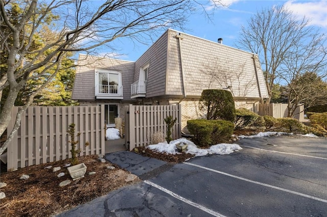 view of home's exterior with mansard roof, a fenced front yard, brick siding, a gate, and uncovered parking