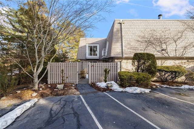 view of side of property featuring brick siding, mansard roof, uncovered parking, a gate, and fence