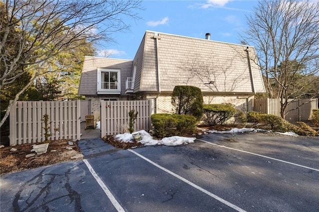 view of side of home featuring uncovered parking, fence, mansard roof, and brick siding