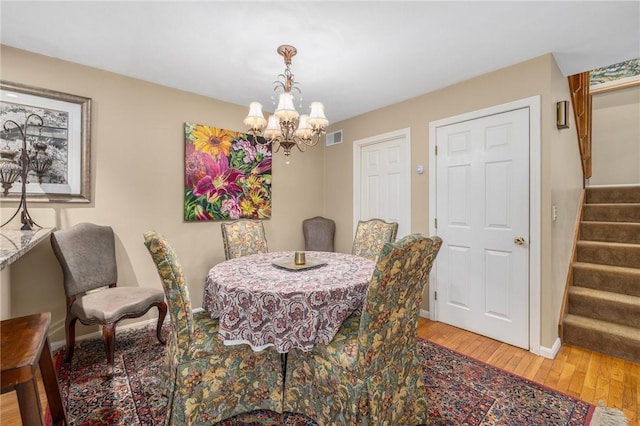 dining room with visible vents, stairway, hardwood / wood-style floors, a chandelier, and baseboards