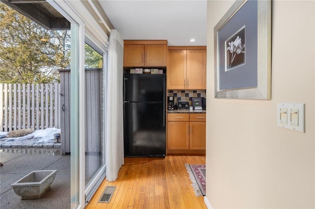 kitchen with tasteful backsplash, visible vents, brown cabinets, freestanding refrigerator, and light wood-type flooring