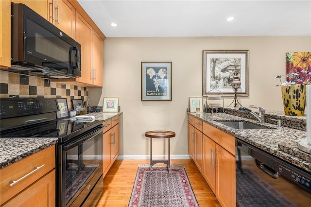 kitchen featuring backsplash, dark stone counters, a sink, light wood-type flooring, and black appliances