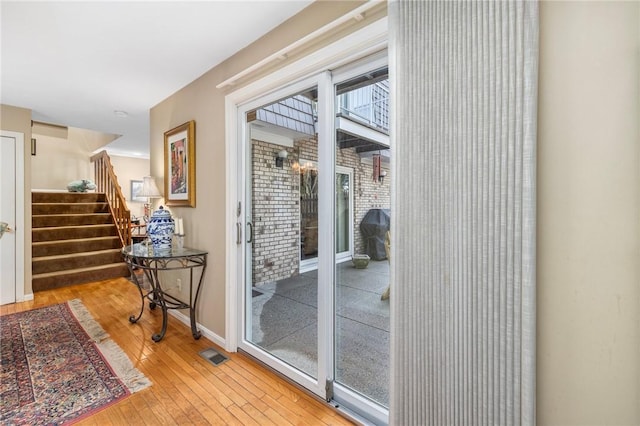 doorway to outside featuring light wood-type flooring, visible vents, stairway, and baseboards