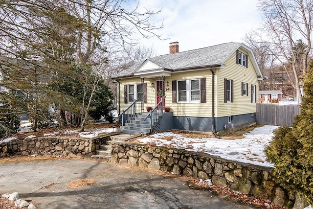 view of front facade featuring a chimney, fence, and roof with shingles