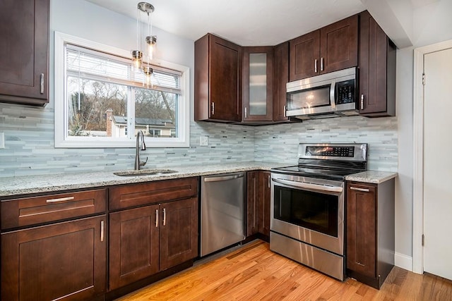 kitchen featuring light stone countertops, glass insert cabinets, stainless steel appliances, and a sink