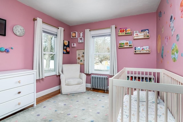 bedroom with radiator, a nursery area, multiple windows, and light wood-style floors