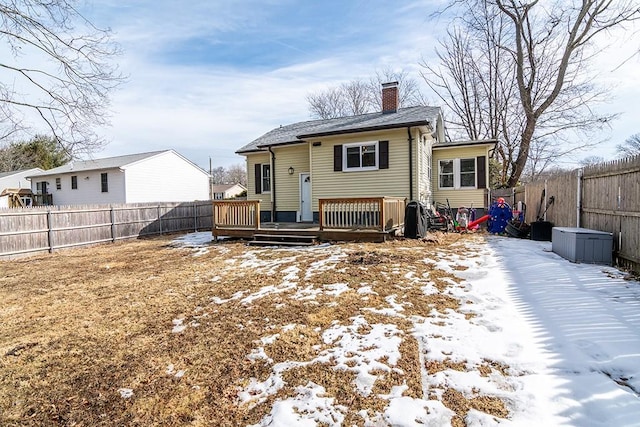 snow covered house with a fenced backyard, a chimney, and a deck