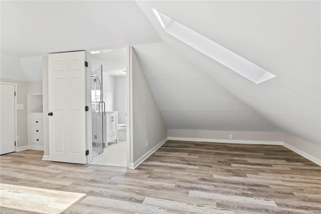 additional living space with vaulted ceiling with skylight, light wood-style flooring, and baseboards