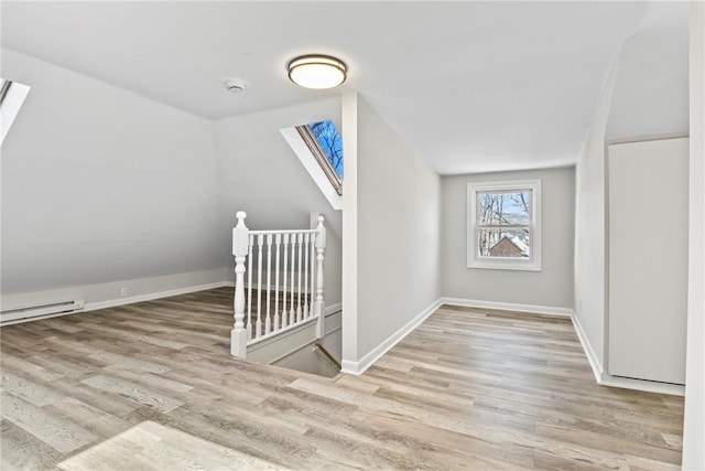 bonus room featuring vaulted ceiling with skylight, light wood-style flooring, baseboards, and baseboard heating