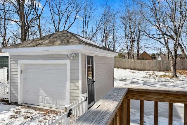 snow covered garage featuring a detached garage and fence