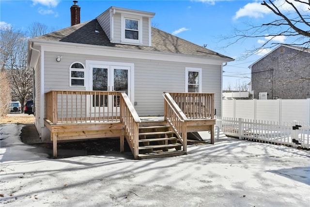 back of property with a deck, roof with shingles, a chimney, and fence