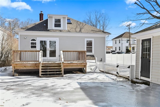 snow covered back of property featuring a chimney, roof with shingles, fence, a deck, and french doors