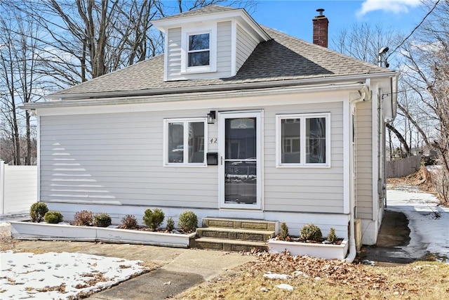 view of front facade featuring entry steps, a shingled roof, a chimney, and fence