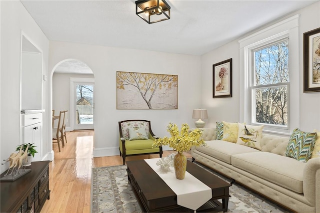 living room featuring light wood-type flooring, baseboards, and arched walkways