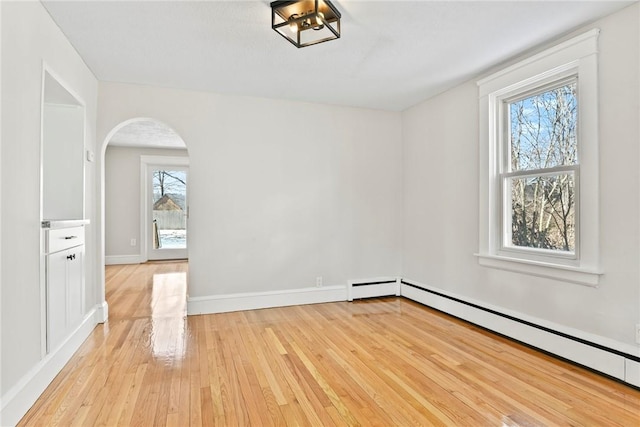 empty room featuring arched walkways, light wood-type flooring, a baseboard radiator, and baseboards