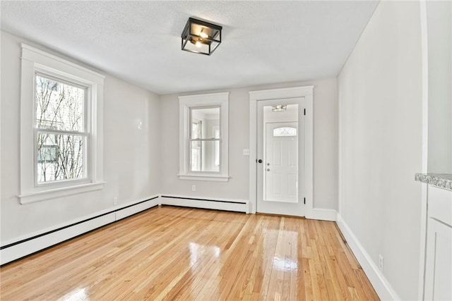 entryway with light wood-type flooring, a baseboard radiator, baseboards, and a textured ceiling