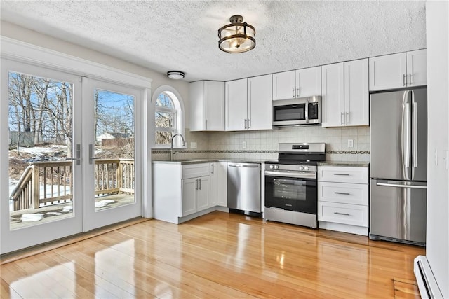 kitchen with appliances with stainless steel finishes, dark countertops, a baseboard radiator, and white cabinets