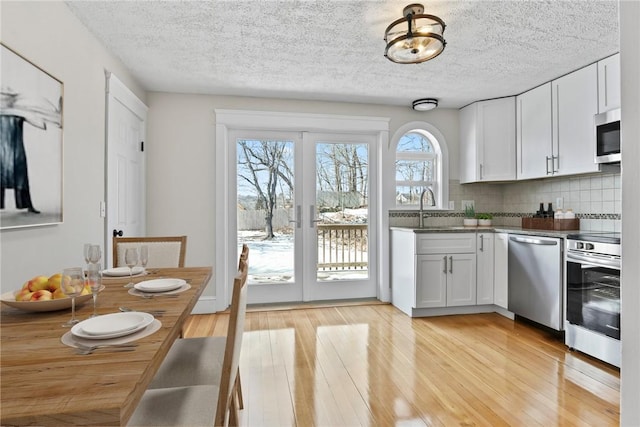 kitchen with appliances with stainless steel finishes, dark countertops, white cabinets, and light wood finished floors