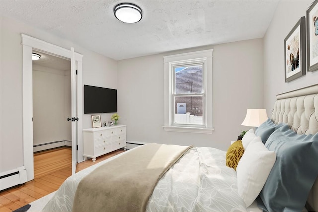 bedroom with a textured ceiling, baseboard heating, and wood finished floors