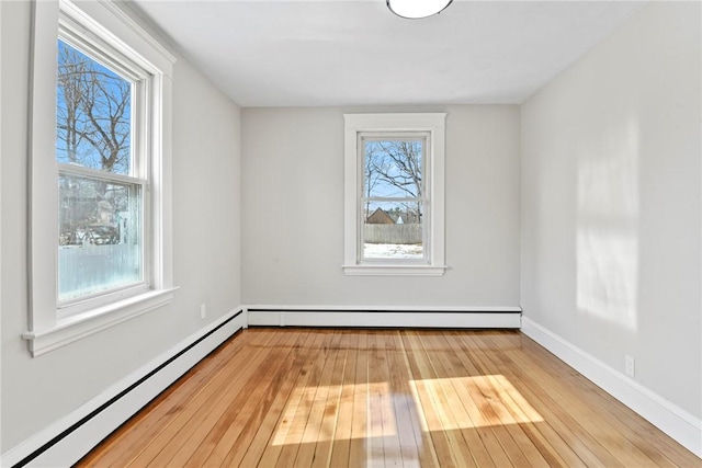 empty room featuring a baseboard heating unit, a healthy amount of sunlight, and hardwood / wood-style flooring