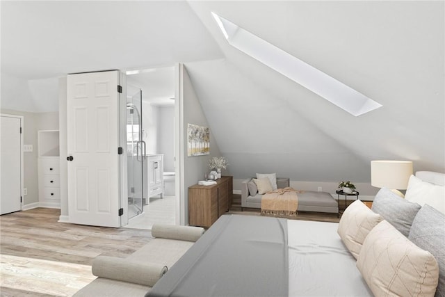 bedroom featuring lofted ceiling with skylight, ensuite bath, and light wood-style floors