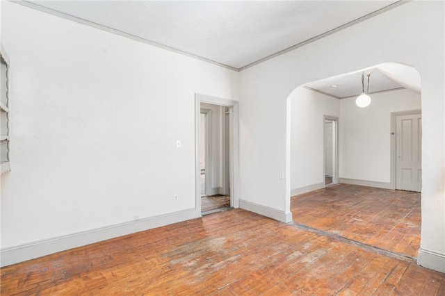 unfurnished room with ornamental molding, arched walkways, wood-type flooring, and baseboards