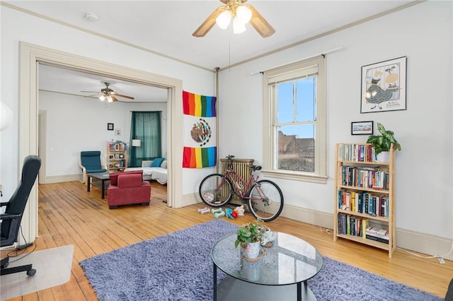 living area with a ceiling fan, wood-type flooring, ornamental molding, and baseboards