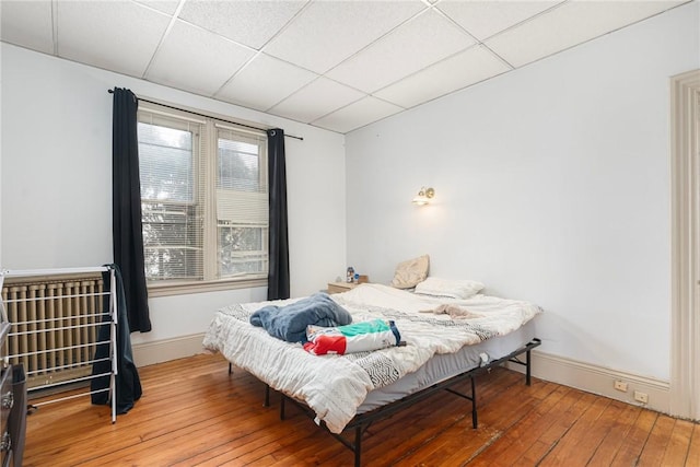 bedroom with hardwood / wood-style floors, a paneled ceiling, and baseboards