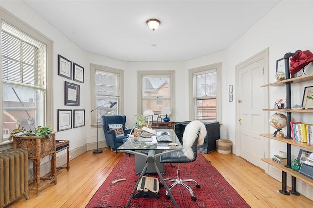 home office with a healthy amount of sunlight, wood-type flooring, baseboards, and radiator heating unit