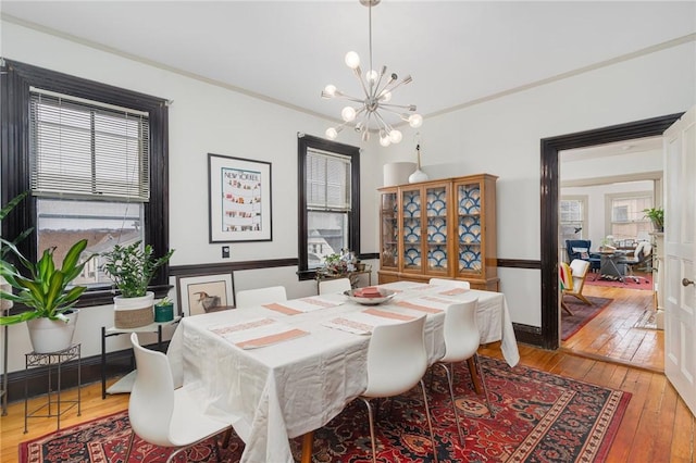 dining area featuring crown molding, light wood-style flooring, and a notable chandelier