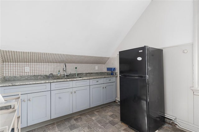 kitchen featuring lofted ceiling, stone finish floor, a sink, and freestanding refrigerator