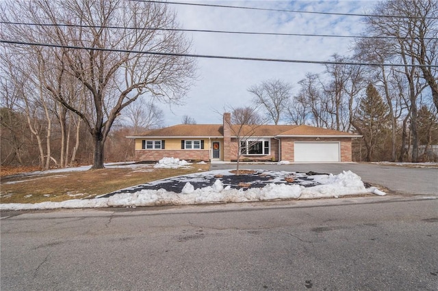 view of front of property with driveway, brick siding, a chimney, and an attached garage