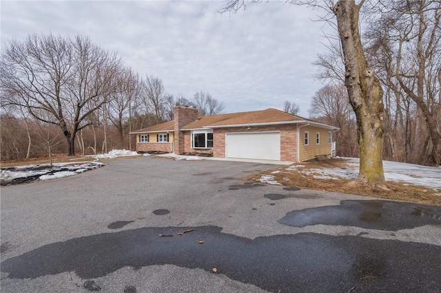 view of front of property featuring an attached garage, driveway, a chimney, and brick siding