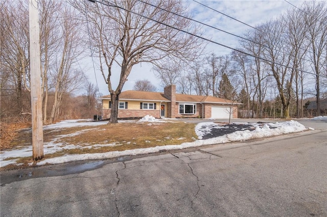 view of front facade featuring driveway, brick siding, a chimney, and an attached garage