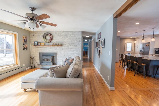 living area with baseboard heating, a wealth of natural light, and light wood-style floors