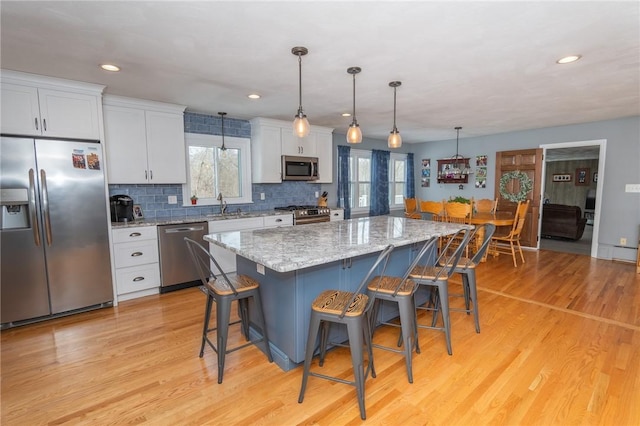 kitchen with stainless steel appliances, a sink, a kitchen island, white cabinets, and pendant lighting