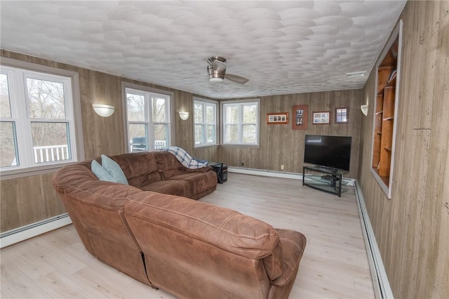 living area with a baseboard radiator, light wood-style flooring, ceiling fan, wood walls, and a baseboard heating unit