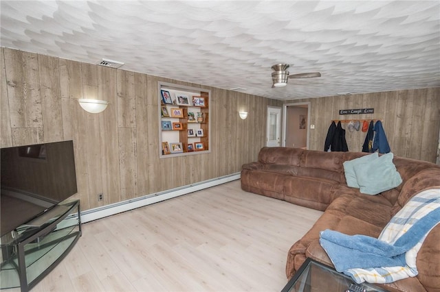 living area featuring light wood finished floors, wood walls, baseboard heating, and visible vents