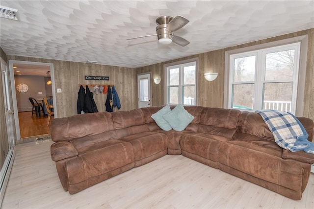 living area featuring wooden walls, visible vents, a baseboard radiator, ceiling fan, and light wood-style floors