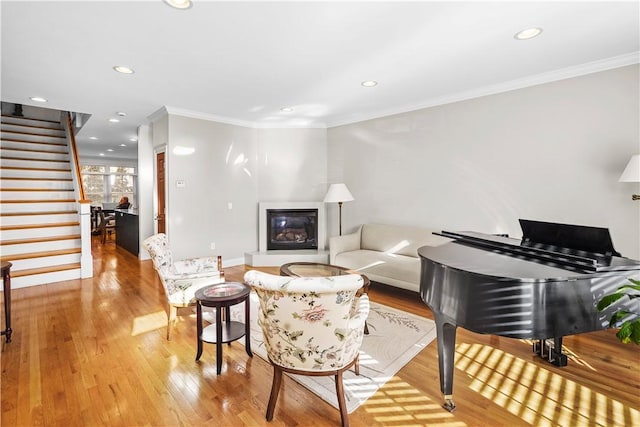 living area featuring light wood finished floors, stairway, ornamental molding, and a glass covered fireplace