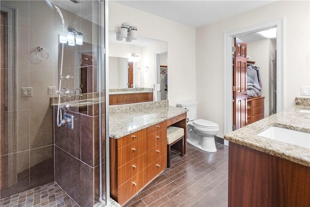 bathroom featuring a walk in closet, toilet, a shower stall, vanity, and wood finished floors